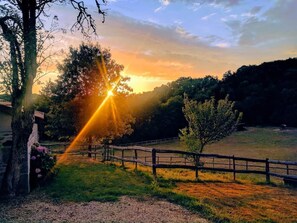 Ein Sonnenuntergang über einer ländlichen Landschaft mit Holzzaun, Bäumen und einem Gebäude mit Blumenkasten.