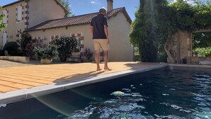 Um homem está em um deck de madeira perto de uma piscina, com uma casa ao fundo.