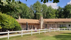 Un edificio a due piani con tetto in tegole, circondato da un recinto bianco e immerso in un ambiente verdeggiante.
