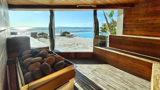 A wooden deck with a stone basin, a view of the ocean, and a clear sky.