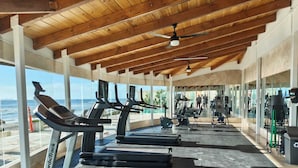 A gym with treadmills, exercise equipment, and large windows overlooking the ocean.