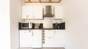 Een compacte keuken met witte kasten, een roestvrijstalen afzuigkap, een magnetron en een vaatwasser.