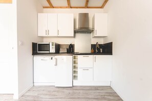 A compact kitchen with white cabinets, a stainless steel range hood, a microwave, and a dishwasher. - Le Gite du Buis - MONTAMISE (MONTAMISE)
