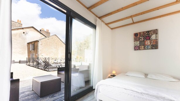 Een slaapkamer met een grote schuifpui die uitkomt op een balkon, een bed met wit beddengoed en een klein nachtkastje met een lamp.