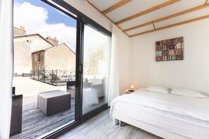 A bedroom with a large sliding glass door leading to an outdoor balcony, a bed with white bedding, and a small bedside table with a lamp. - Le Gite du Buis - MONTAMISE (MONTAMISE)