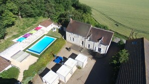 Vista aérea de uma propriedade com piscina, um edifício grande de pedra e vegetação ao redor.