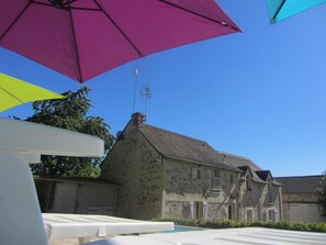 A stone building with a sloped roof, a satellite dish, and a pool area with umbrellas. - Le Vallon - MONDION - Gîte (MONDION)