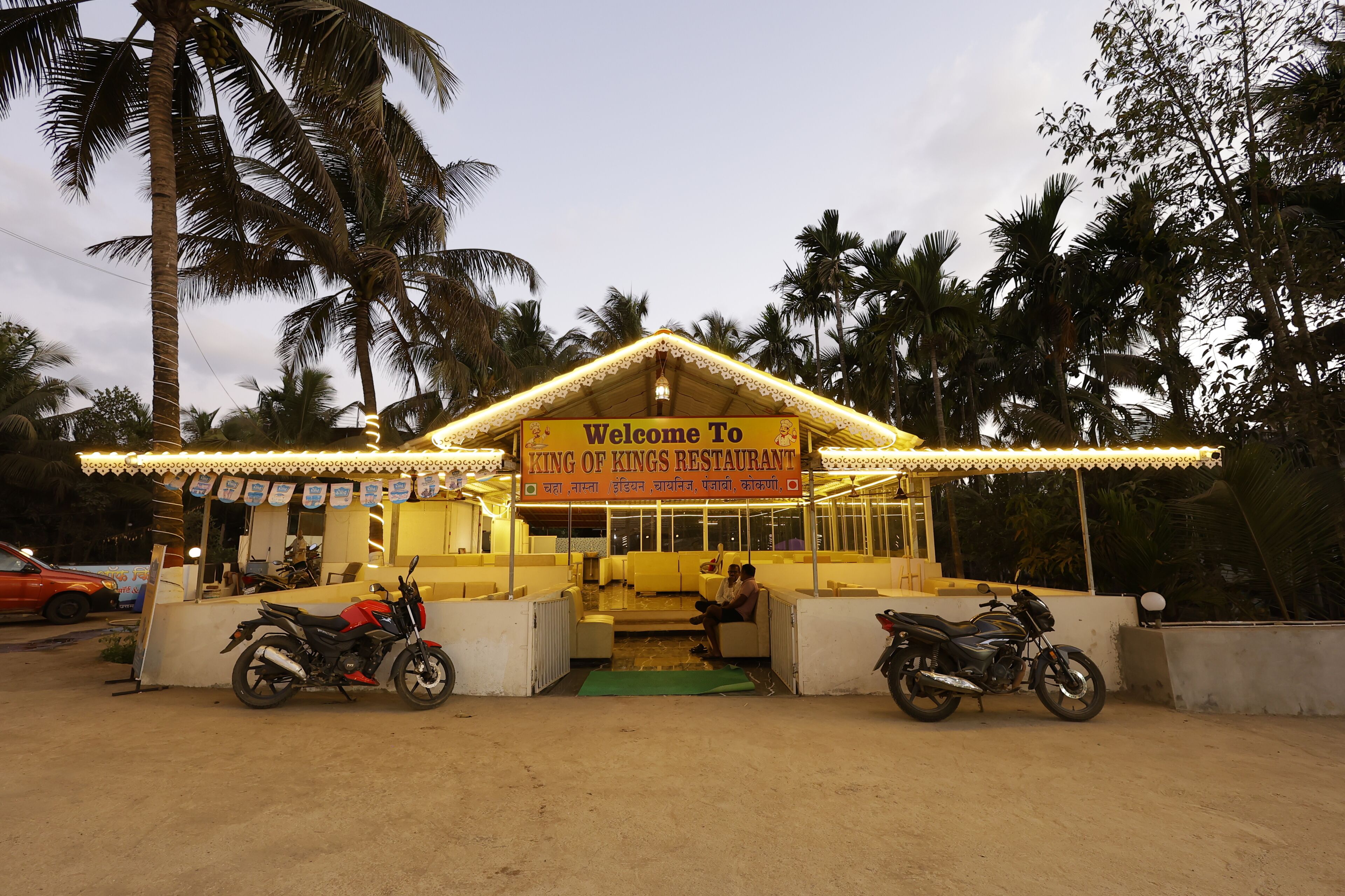 A restaurant named 'King of Kings Restaurant' with a signboard, two motorcycles parked in front, and palm trees in the background.