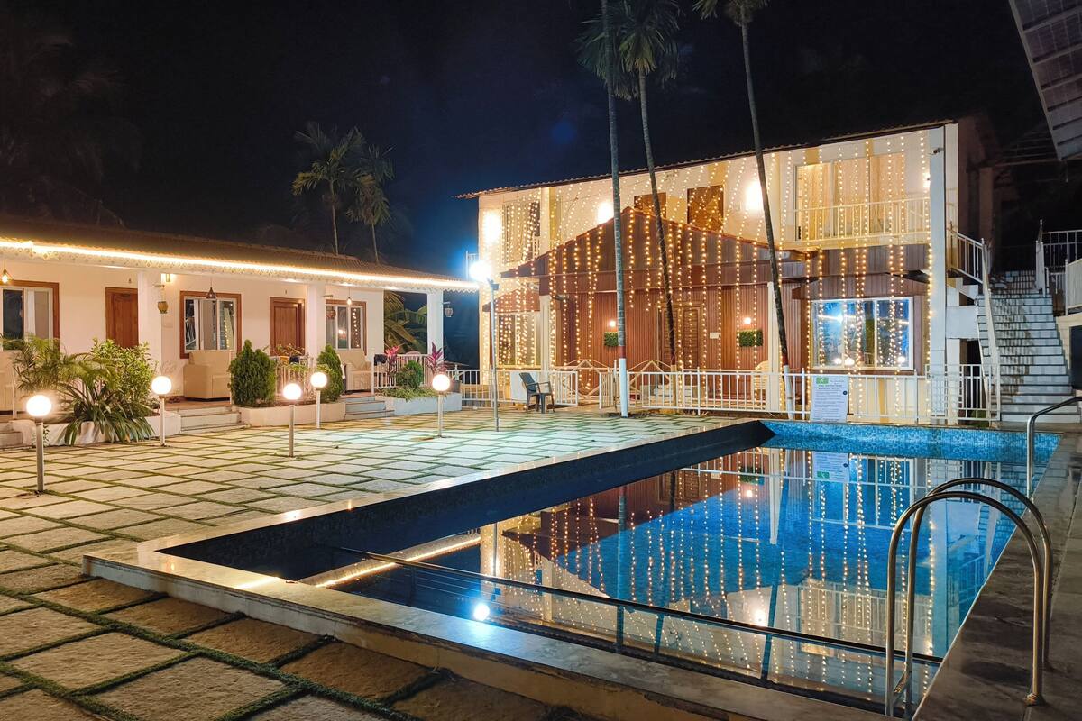 A pool area with a glass barrier, a building with string lights, and a staircase leading to an upper level.