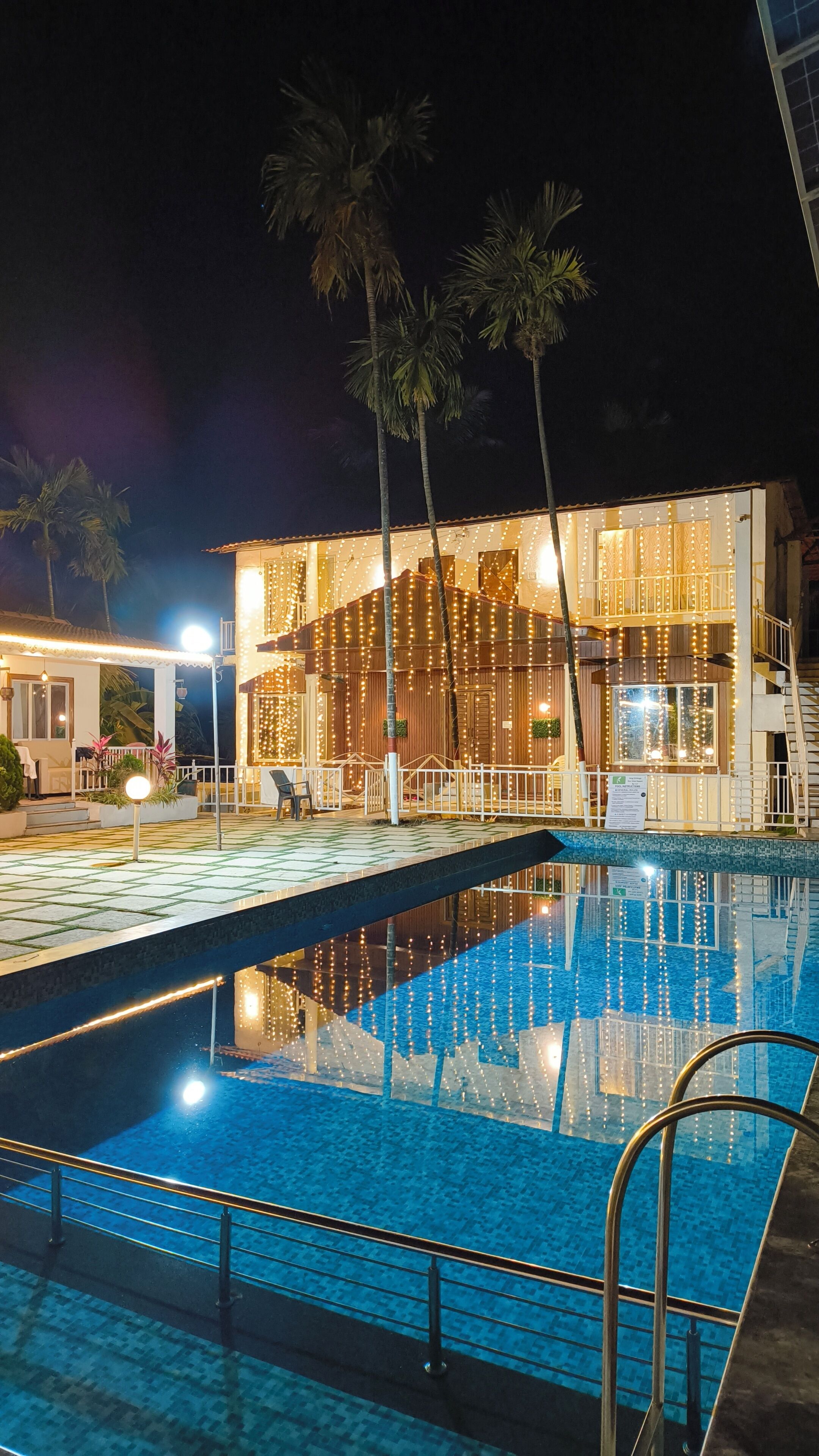 Una piscina con vista a un edificio con luces colgantes y palmeras.