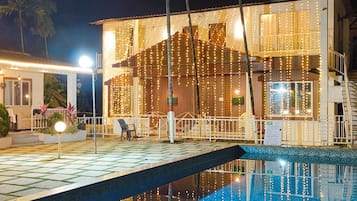 Una piscina con vista a un edificio con luces colgantes y palmeras.