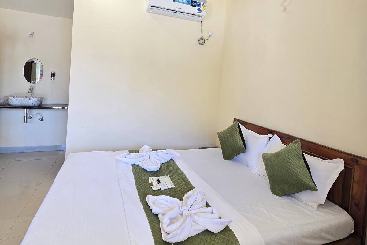 A hotel room with a bed, a bedside table, a mirror, a sink, and an air conditioning unit.