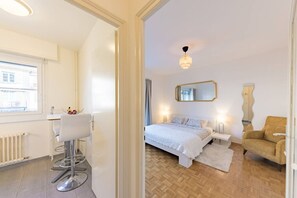 Ein Schlafzimmer mit Bett, Nachttischen, einem Spiegel, einem Sessel und einem Fenster.