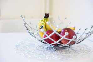 Uma cesta de arame com bananas e maçãs sobre uma superfície de vidro transparente.