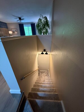 A carpeted staircase with a handrail, a ceiling fan, and a wall-mounted light fixture. - Hot Springs Village Renovated Townhome Retreat (Hot Springs Village)