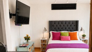A modern bedroom with a large bed, bedside tables, a TV, and a kitchen area with a sink and cabinets. - Frida's Favorite Loft in Coyoacan, walk to Frida Kahlo's "Casa Azul" Museum. (Ciudad de México)