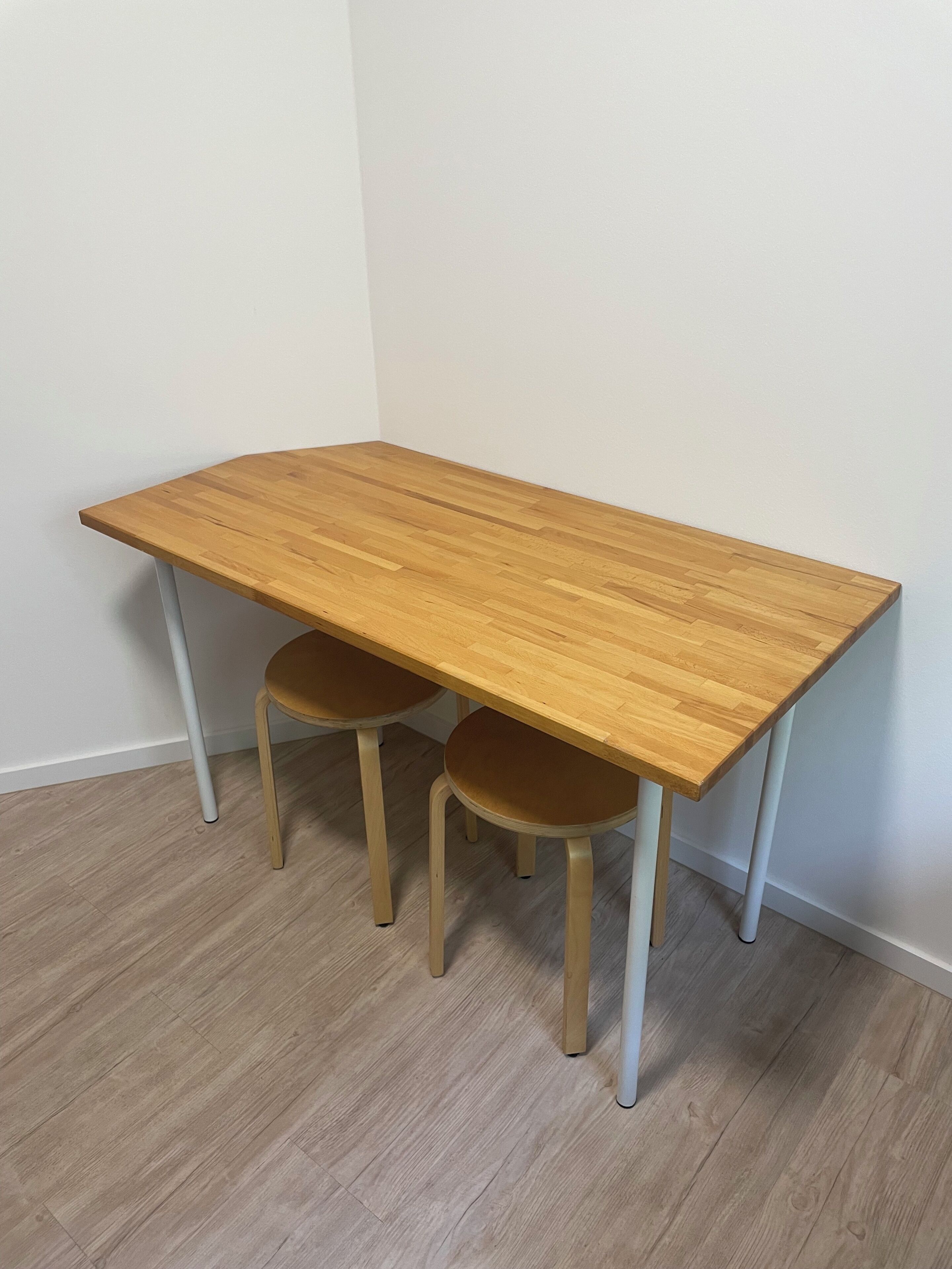 Ein rechteckiger Holztisch mit zwei Stühlen, eine weiße Wand und ein Holzboden.