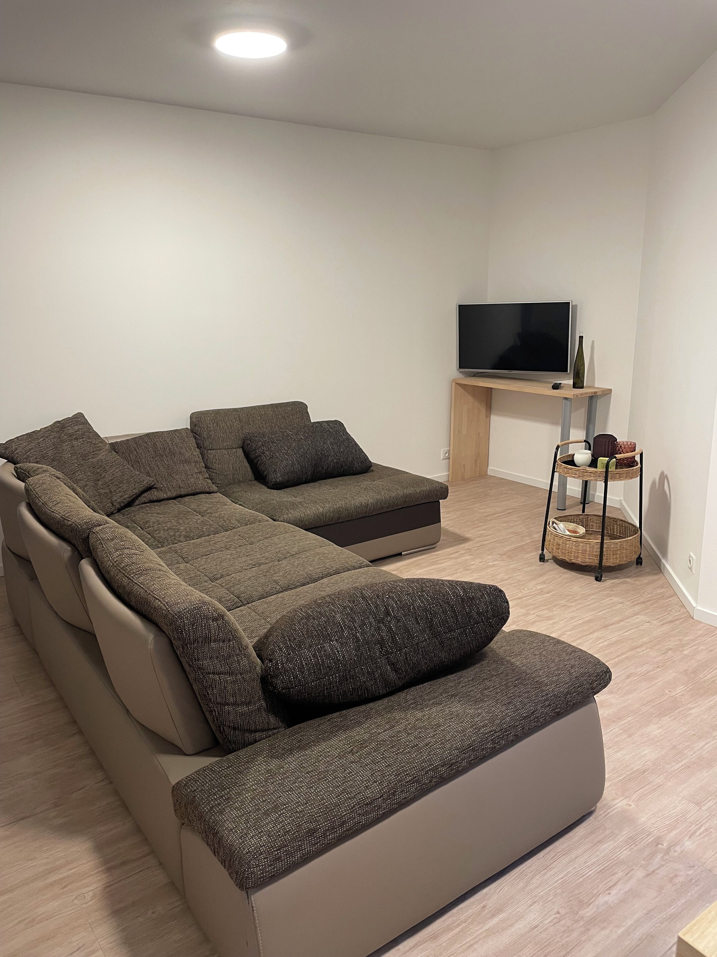 A modern living room with a sectional sofa, a flat-screen TV on a wooden stand, and a wicker basket on a small table.