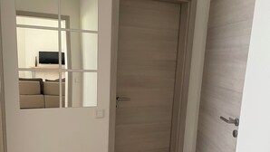 Un pasillo con piso de madera, una puerta espejada y una puerta cerrada.