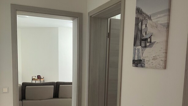 Un pasillo con piso de madera, un sofá gris y un cuadro en la pared.