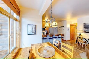 A dining area with a wooden table, chairs, and a hanging light fixture. - Ski-In/Out Condo w/ Fireplace + Dogs OK (Whitefish)