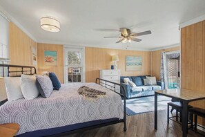 Ein Schlafzimmer mit einem Bett, einem Schreibtisch, einem Stuhl, einem Deckenventilator und einem Fenster mit Jalousien.
