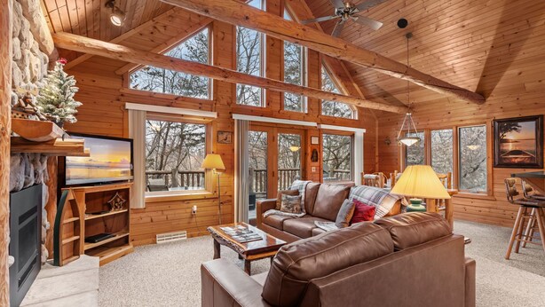Een vakantiehuisje in houtstijl met een open haard, leren bank, houten planken en grote ramen.