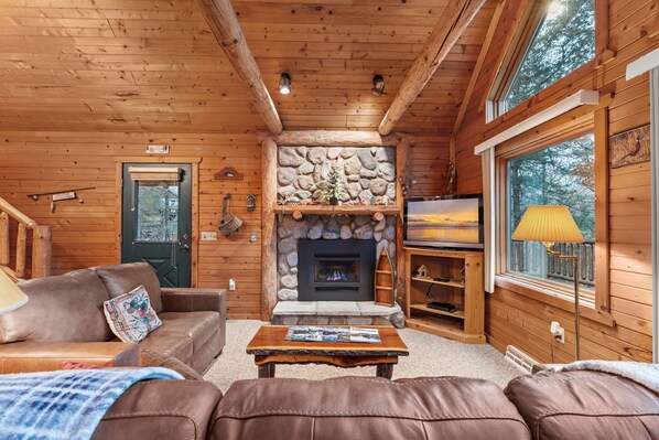 A cozy cabin interior with a stone fireplace, wooden walls, a television, and a comfortable seating area.