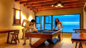 Une table de billard dans une pièce dotée de grandes fenêtres donnant sur la mer, de meubles en bois et d’un aménagement intérieur moderne.