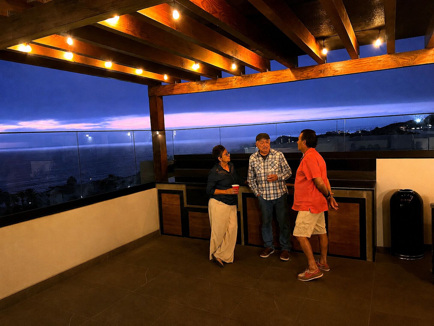 A balcony with a view of the ocean at dusk, wooden beams, and a trash can.