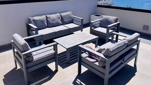 Une terrasse sur le toit, aménagée avec un ensemble de canapés, une table et des chaises, d’où l’on peut admirer la mer.