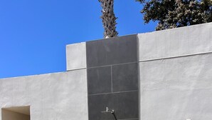 Un espace de douche extérieur moderne, avec un mur carrelé, un robinet et de la verdure tout autour.