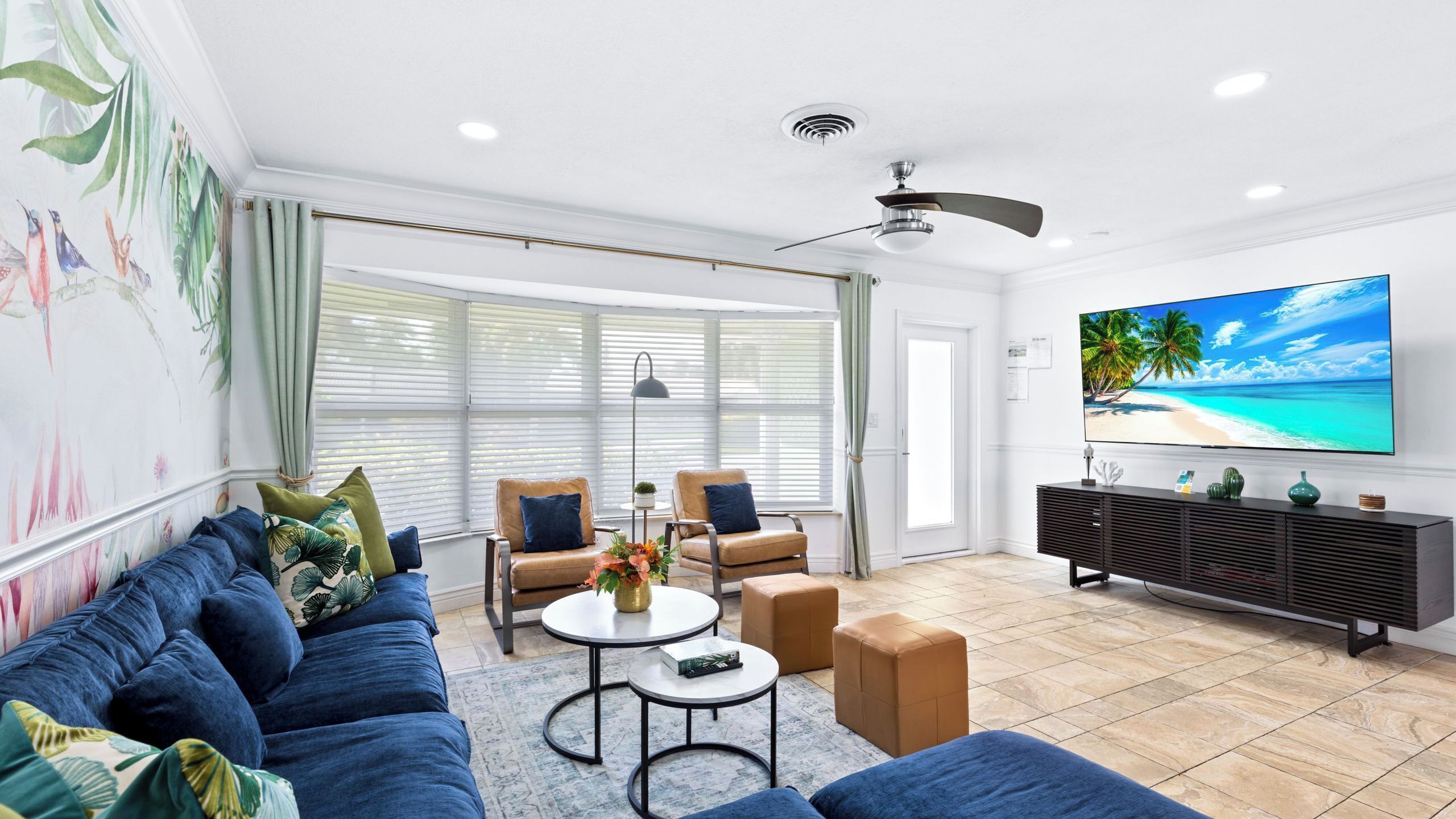 A living room with a sofa, chairs, a coffee table, a TV, and a ceiling fan.