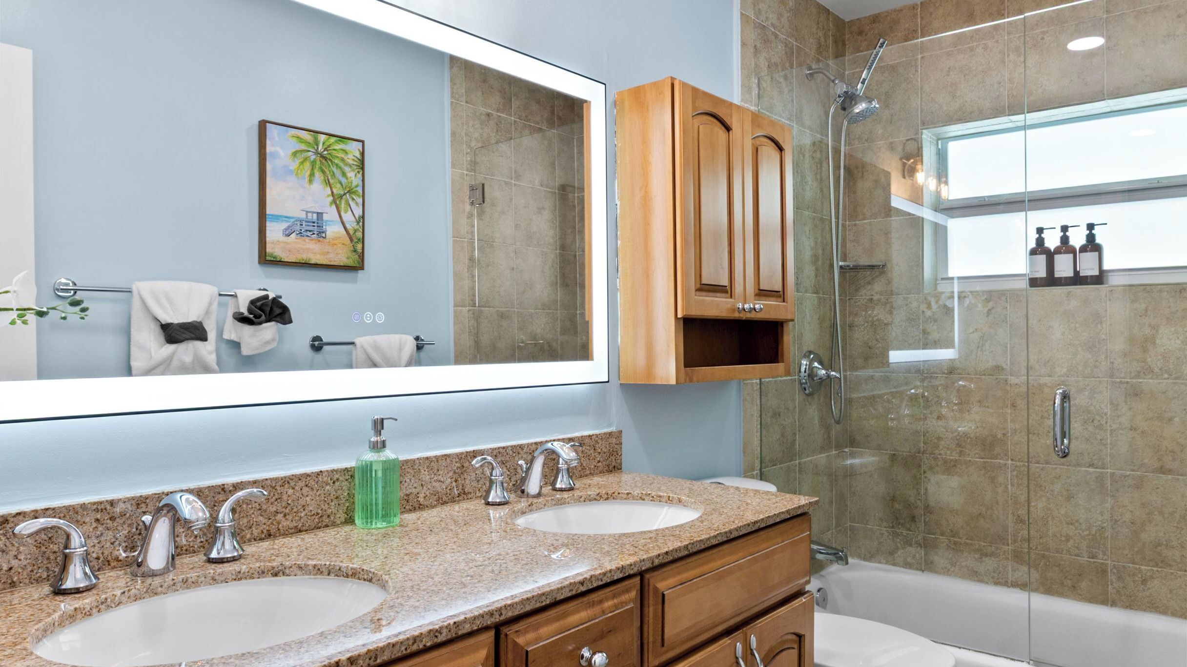 A modern bathroom with two sinks, a large mirror, wooden cabinets, and a shower.
