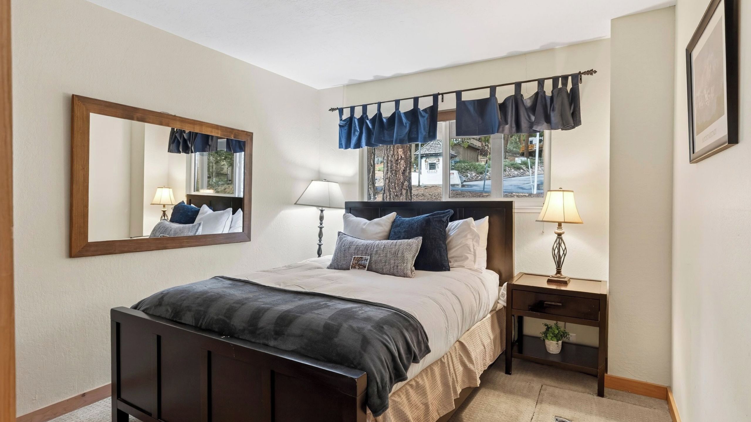 A bedroom with a bed, bedside tables, a lamp, a mirror, and a window with curtains.