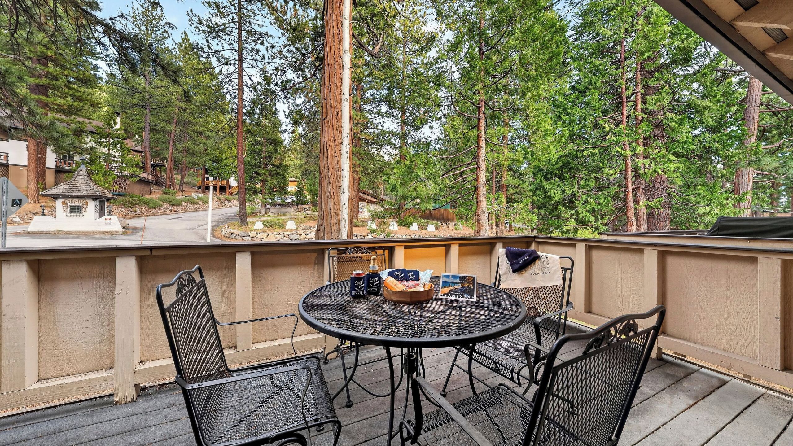 A covered outdoor patio with a round table and chairs, surrounded by tall trees.