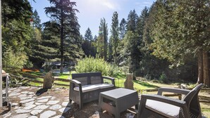 Un patio al aire libre con mobiliario de mimbre, piso de piedra y vista a un área boscosa.