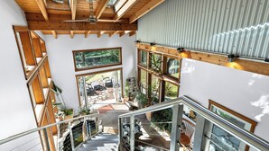 Un interior de varios niveles con vigas de madera, ventanas amplias y una escalera.