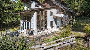 Una casa de dos pisos con base de piedra, ventanas amplias y una terraza de madera.