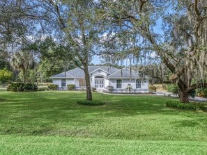 A house with a front lawn, a driveway, and a large tree in the foreground. - Private 3/2 5 min from WEC Ocala (Ocala)