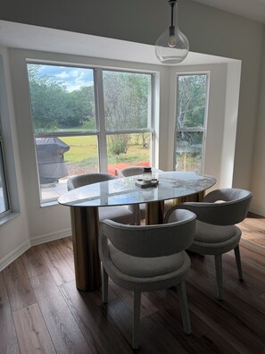 A dining area with a round table, four grey chairs, and large windows offering a view of a yard. - Private 3/2 5 min from WEC Ocala (Ocala)