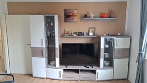 Un espai vital reduït amb televisió integrada, armaris d'emmagatzematge i una estanteria amb objectes decoratius.