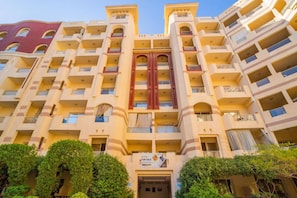 Ein mehrstöckiges Hotel mit zentralem Eingang, Balkonen auf jeder Etage und Bepflanzung davor.