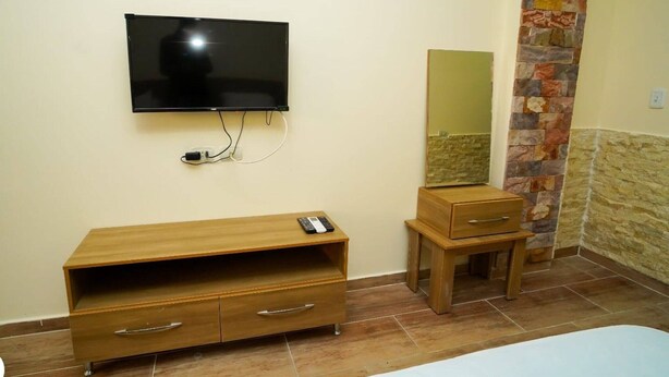 A room with a TV mounted on the wall, a wooden dresser with drawers, a small wooden table, a mirror, and a stone accent wall. - Room-florence Khamsin Hurghada K203 (Hurghada)