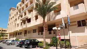 A multi-story hotel with balconies, parked cars, and a palm tree. - Room-florence Khamsin Hurghada K203 (Hurghada)