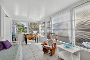Ein helles Zimmer mit einem Bett, einem Sessel, einem Kicker und einem Fenster mit Jalousien.
