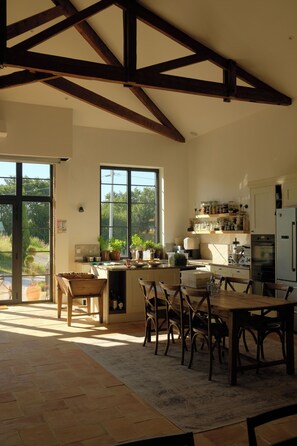 A spacious kitchen with wooden beams, large windows, and a dining area with chairs and a table. - Luxury Private Estate in Gascony | Heated Pool, Spa, Air Conditioning, Sleeps 14 (Saint-Mézard)