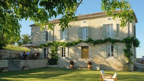 Un bâtiment en pierre avec un toit en tuiles, une porte en bois et un petit porche doté de sièges pour l’extérieur.