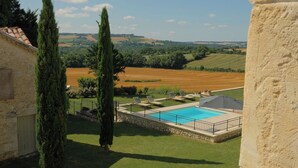 Une piscine dotée d’une plage en pierre, entourée d’une pelouse et de cyprès, et offrant une vue sur des collines ondoyantes à l’arrière-plan.