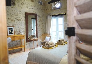 A bedroom with a bed, a wooden dresser, a chair, a mirror, and a window. - Luxury Private Estate in Gascony | Heated Pool, Spa, Air Conditioning, Sleeps 14 (Saint-Mézard)